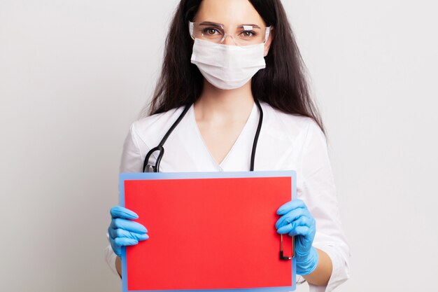 Junge Ärztin in einer Maske hält ein leeres Blatt Papier
