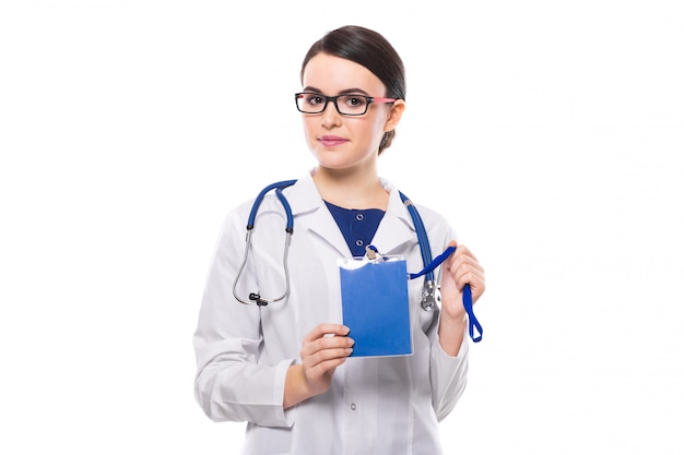Junge Ärztin mit dem Stethoskop, das blauen Ausweis in ihren Händen in der weißen Uniform hält