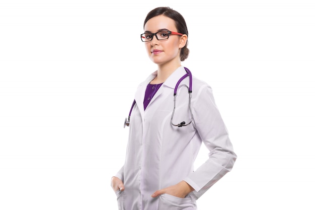 Junge Ärztin mit dem Stethoskop, das ihre Hände in den Taschen in der weißen Uniform hält