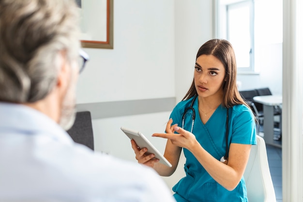 Junge Ärztin und älterer Mann, die in einem Wartezimmer im Krankenhaus kommunizieren. Konzept für Medizin, Gesundheitswesen und Menschen - Arzt- und Patiententreffen im Krankenhaus