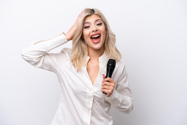 Junge Sängerin, die ein Mikrofon isoliert auf weißem Hintergrund mit Überraschungsausdruck aufhebt