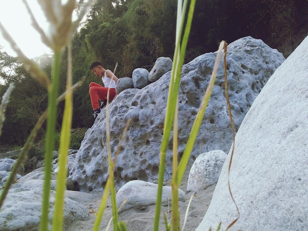 Foto junge schaut nach unten, während er auf einem felsen sitzt