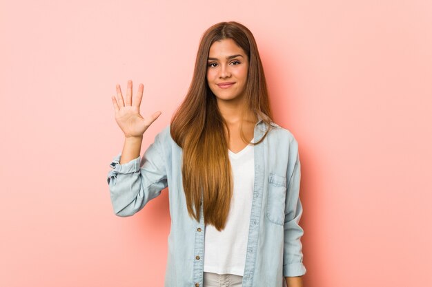 Junge schlanke Frau, die fröhlich lächelt und Nummer fünf mit den Fingern zeigt.