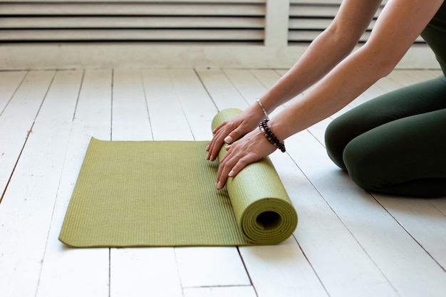Junge schlanke Frauenhände drehen grüne Matte für Fitness oder Yoga auf weißem Holzboden
