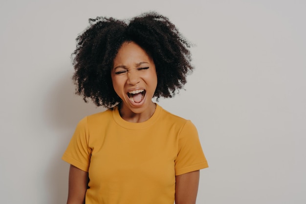 Junge schöne Afrikanerin mit lockigem Haar, die ein lässiges gelbes T-Shirt trägt und vor Wut schreit