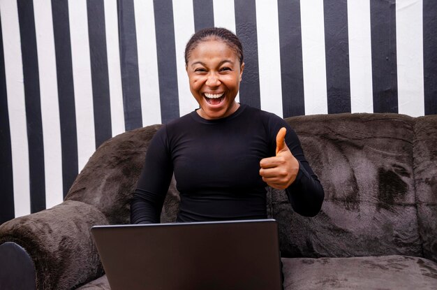 Junge schöne afrikanische Dame fühlte sich überwältigt von dem, was sie auf ihrem Laptop sah und Daumen nach oben machte