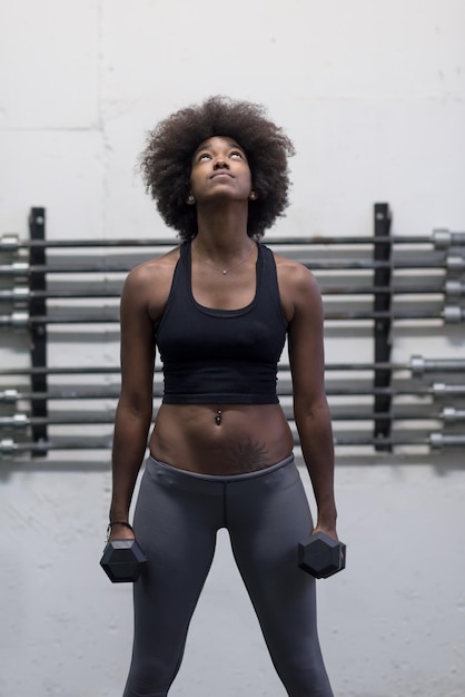 junge schöne Afroamerikanerin, die Bizeps-Curls in einem Fitnessstudio macht