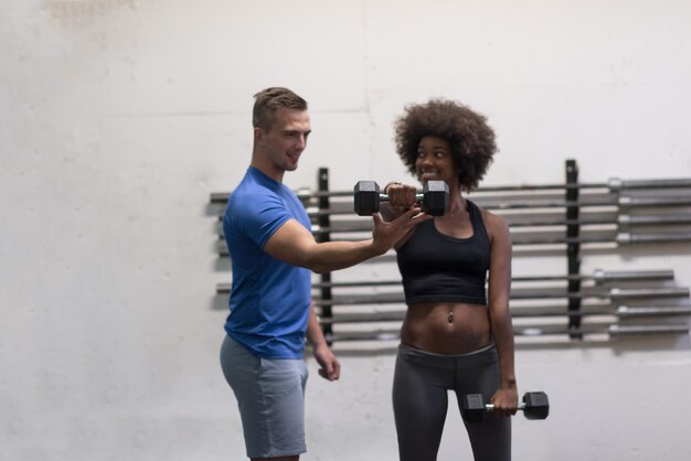 junge schöne Afroamerikanerin, die Bizeps-Curls mit Fitnesstrainer in einem Fitnessstudio macht