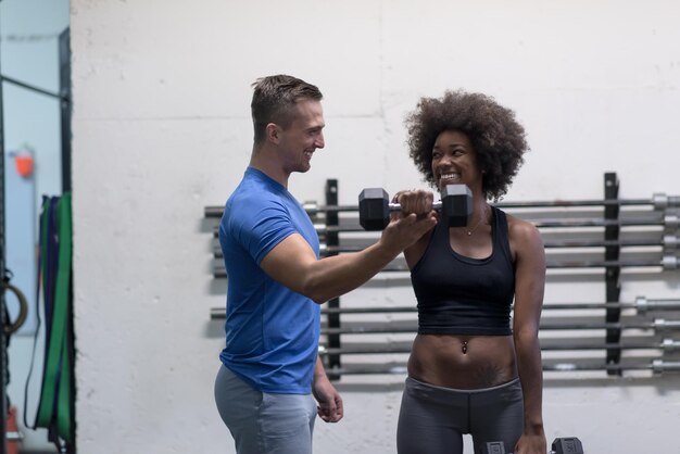junge schöne Afroamerikanerin, die Bizeps-Curls mit Fitnesstrainer in einem Fitnessstudio macht