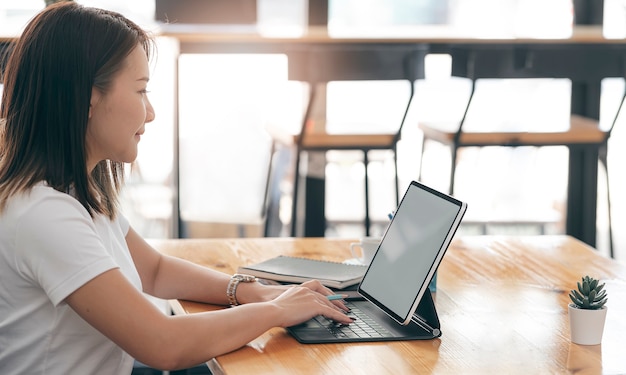 Junge schöne asiatische Frau, die auf Tablet-Computer beim Sitzen am Co-Arbeitsbereich arbeitet.