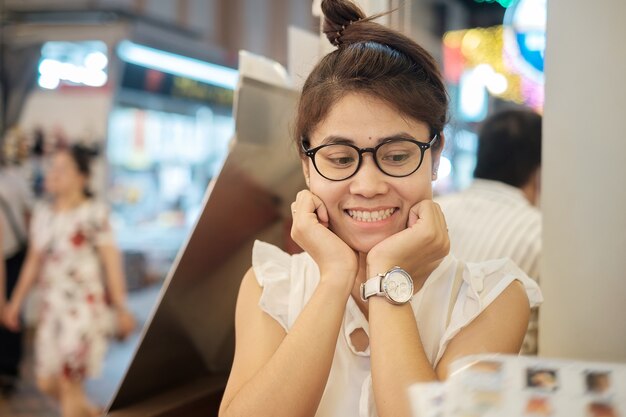 Junge schöne asiatische Frau, die beim Schauen der Menüabendessenzeit im Restaurant oder in der Kaffeestube lächelt