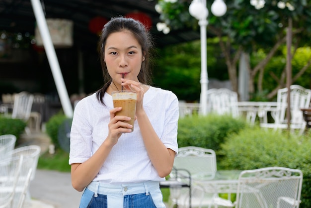 Junge schöne asiatische Frau, die Kaffee am Kaffeehaus draußen trinkt