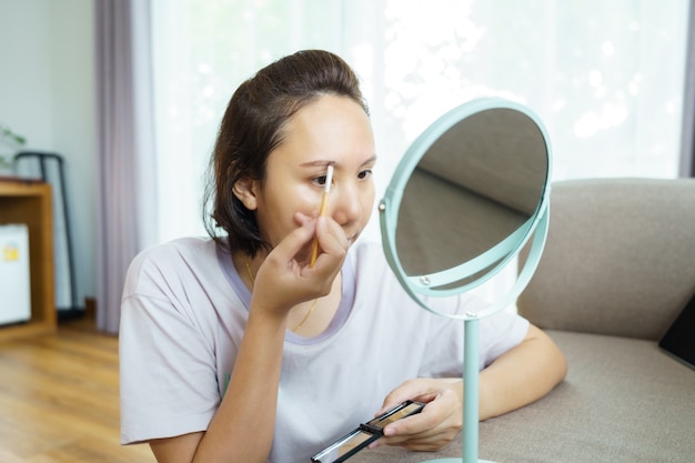 Junge schöne asiatische Frau, die vorne einen Spiegel zu Hause anwendet. Malerei Kosmetik