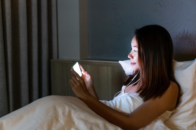 Junge schöne asiatische Frau im Bett mit Handy spät in der Nacht im dunklen Schlafzimmer Smartphone Internetsucht Schlaflosigkeit Konzept