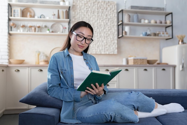 Junge schöne asiatische frau in den gläsern und im jeanshemd, die zu hause studieren, glückliche studentin, die lächelt