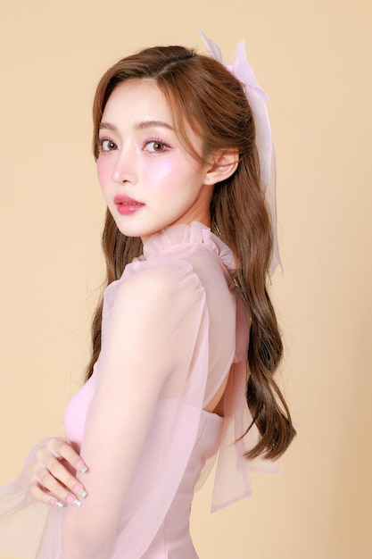 Junge schöne asiatische Frau in einem rosa eleganten Kleid, koreanisches Make-up, feuchtig, glatte, perfekte Haut auf einem beige Hintergrund, Gesichtsbehandlung, Kosmetik, plastische Chirurgie.