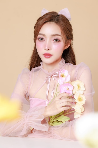 Junge schöne asiatische Frau in einem rosa eleganten Kleid, koreanisches Make-up, feuchtig, glatte, perfekte Haut mit Blumen auf beige Hintergrund, Gesichtsbehandlung, Kosmetik, plastische Chirurgie