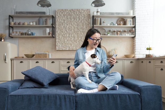 Junge schöne asiatische Frau mit Jack-Russell-Terrier, die per Videoanruf mit einer Frau von Freunden spricht