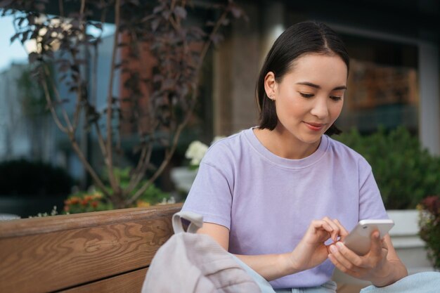 Junge schöne asiatische Frau mit mobiler App, die online auf der Straße einkauft