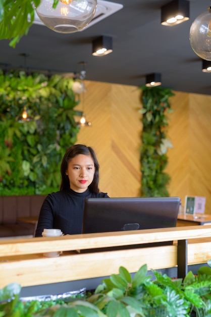 Junge schöne asiatische Geschäftsfrau, die Laptop am Kaffeehaus verwendet