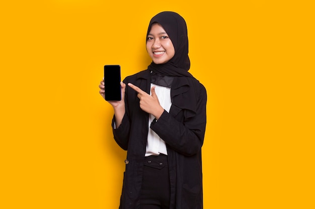 junge schöne asiatische muslimische geschäftsfrau, die handy auf gelbem hintergrund demonstriert
