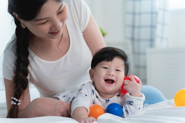 Junge schöne asiatische Mutter mit ihrem kleinen netten Baby auf Bett.