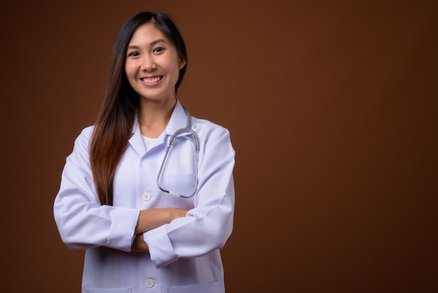 Junge schöne asiatische Ärztin vor braunem Hintergrund