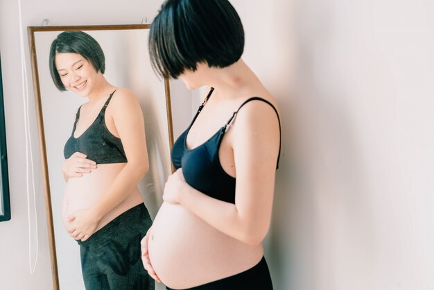 Junge schöne asiatische schwangere Frau, die zu Hause ihren Bauch berührt