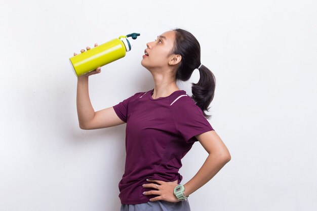 Junge schöne asiatische Sportfrau trinkt Wasser nach dem Training auf weißem Hintergrund