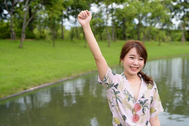 Junge schöne asiatische Touristenfrau, die am Park entspannt