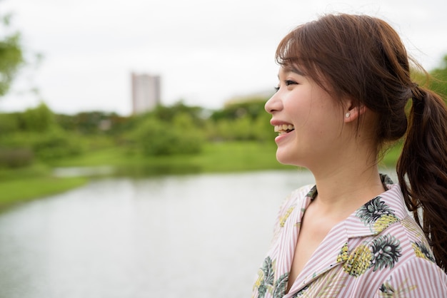 Junge schöne asiatische Touristenfrau, die am Park entspannt