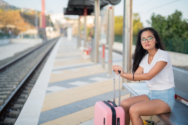 Junge schöne asiatische Touristenfrau, die beim Warten am Bahnhof sitzt