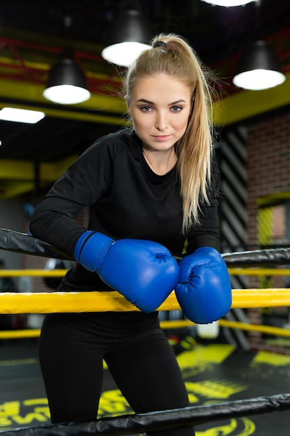 Junge schöne Athletin in blauen Boxhandschuhen posiert im Ring und schaut in die Kamera