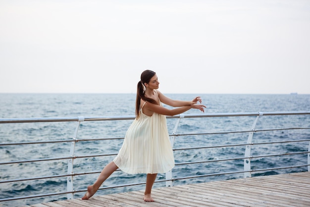 Junge schöne Ballerina, die außerhalb des Meereshintergrundes tanzt und posiert
