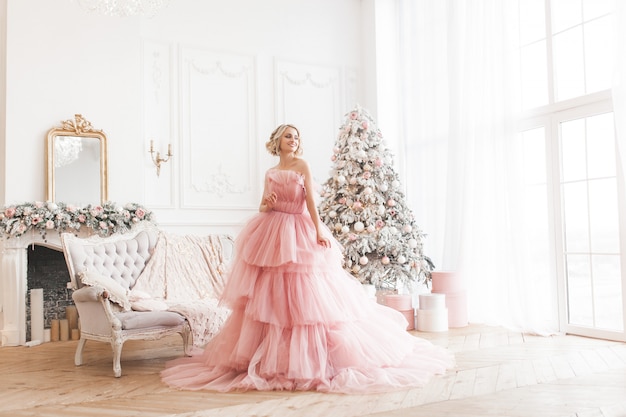 Junge schöne blonde Frau auf voller Höhe der Weihnachtsszene. Attraktive Dame im rosa wunderschönen Kleid.