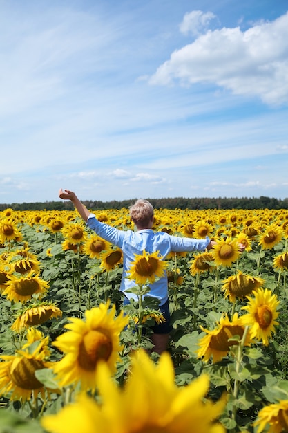 Junge schöne blonde Frau, die im Sonnenblumenfeld steht