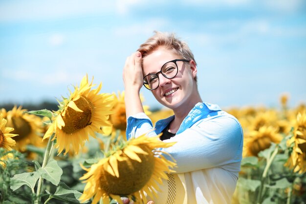 Junge schöne blonde Frau, die im Sonnenblumenfeld steht