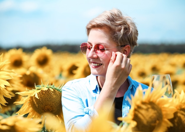 Junge schöne blonde Frau, die im Sonnenblumenfeld steht