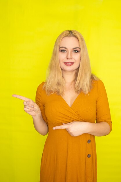 Junge schöne blonde Frau im dunkelgelben Kleid, das über gelbe Wand innen aufwirft