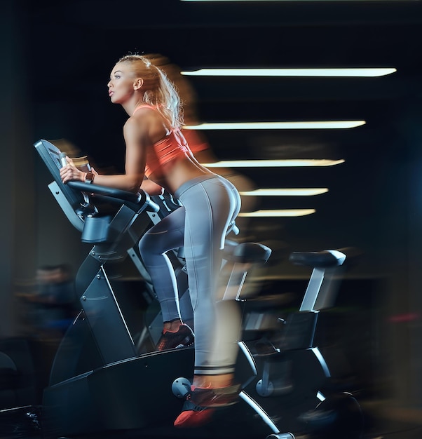 Junge schöne blonde Frau im Sportbekleidungstraining auf einem Heimtrainer in einem modernen Fitnesscenter.