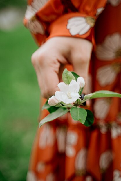 Junge schöne blonde Frau in blühendem Garten. Frühlingsbäume in voller Blüte. Orange Kleid und Strohhut.