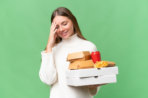 Junge schöne blonde Frau mit Essen zum Mitnehmen vor isoliertem Hintergrund lachend