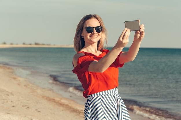 Junge schöne blonde Frau mit Handy am Strand