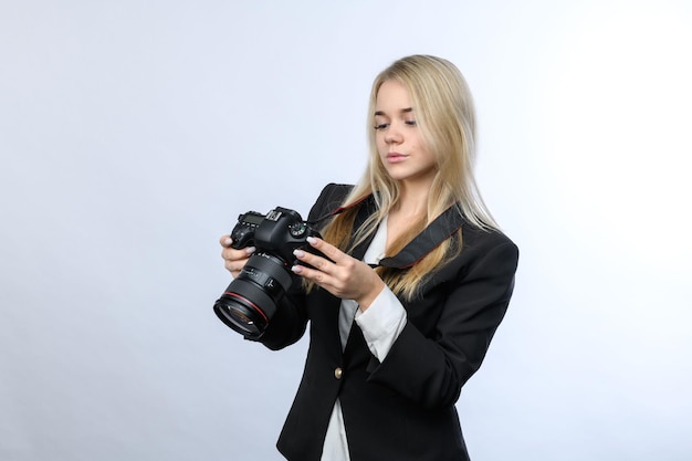 Junge schöne blonde Frau mit modernen DSLR-Kameras, die zum Kamerabildschirm auf weißem Hintergrund schauen