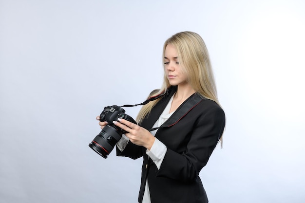 Junge schöne blonde Frau mit modernen DSLR-Kameras, die zum Kamerabildschirm auf weißem Hintergrund schauen