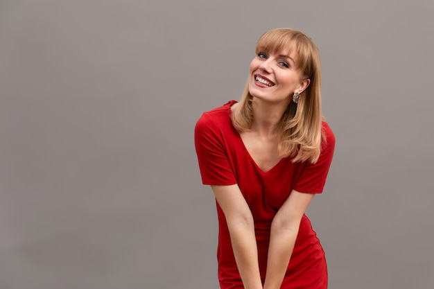 Junge schöne blonde Frau mit stylischem rotem Kleid auf grauem Wandhintergrund Leeren Platz für Text kopieren