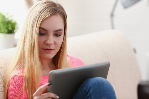 junge schöne blonde Frau sitzen auf dem Sofa im Wohnzimmer halten Tablette in den Armen