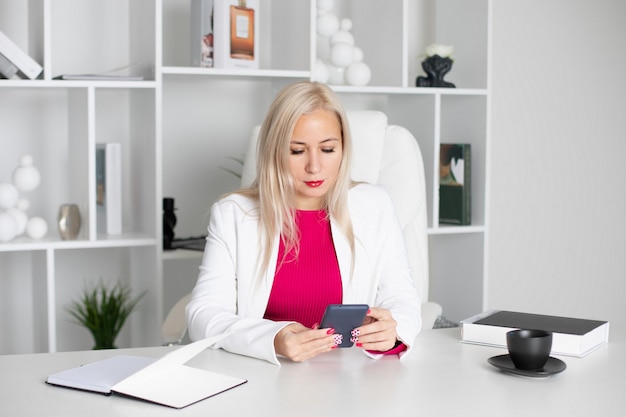 Foto junge schöne blonde geschäftsfrau in weißer jacke sitzt im büro bei der arbeit