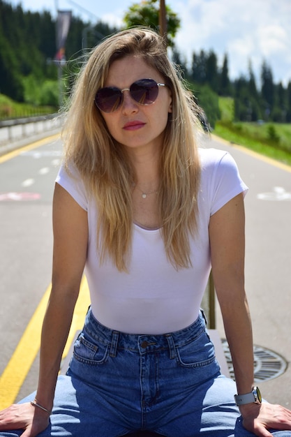 Junge schöne blonde weiße Frau in weißer T-Shirt Sonnenbrille und Jeans