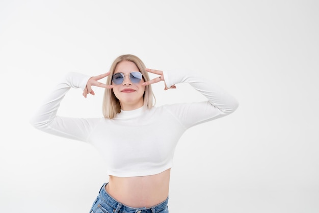 Junge schöne Blondine in einem weißen Top auf einem weißen, isolierten Hintergrund. Positiver und selbstbewusster Mensch